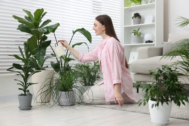 Photo of Beautiful young woman watering green houseplants at home