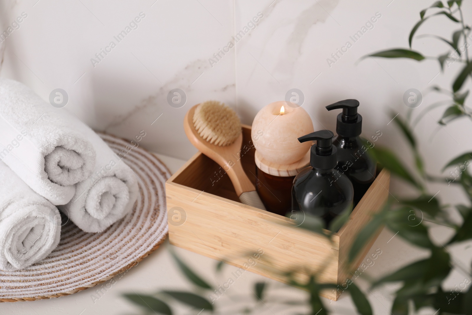 Photo of Wooden box with different toiletries, burning candle and clean towels on countertop in bathroom