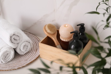 Photo of Wooden box with different toiletries, burning candle and clean towels on countertop in bathroom