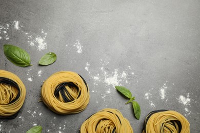 Photo of Raw linguine pasta with basil on grey table, flat lay. Space for text