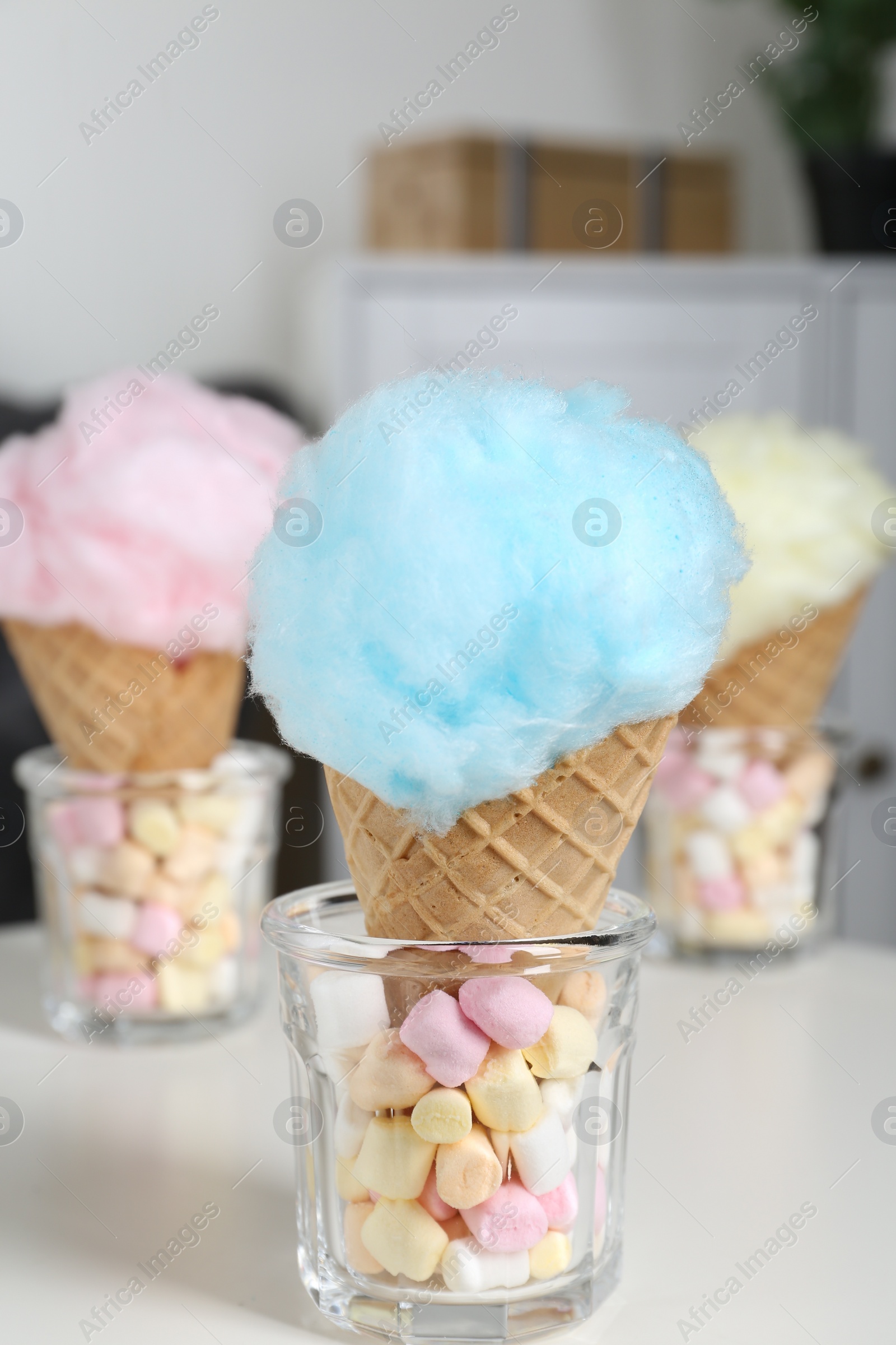 Photo of Sweet cotton candies in waffle cones and marshmallows on white table indoors, closeup