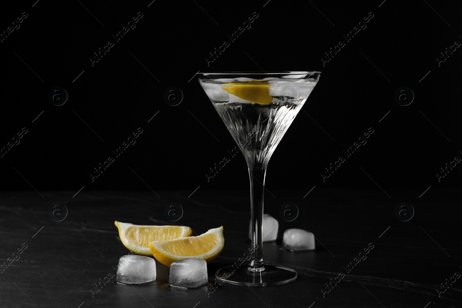 Photo of Martini glass of refreshing cocktail with lemon and ice cubes on black textured table