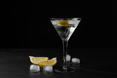 Photo of Martini glass of refreshing cocktail with lemon and ice cubes on black textured table
