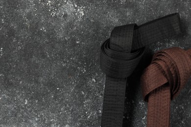 Photo of Black and brown karate belts on gray textured background, flat lay. Space for text