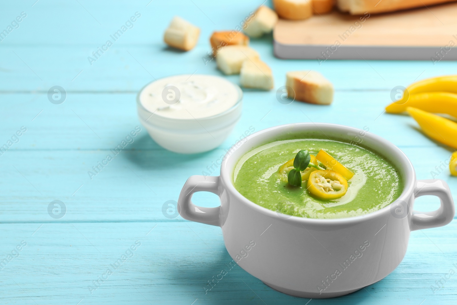 Photo of Bowl of broccoli cream soup with chili pepper served on blue wooden table. Space for text