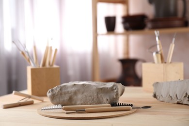 Photo of Clay and set of modeling tools on wooden table in workshop