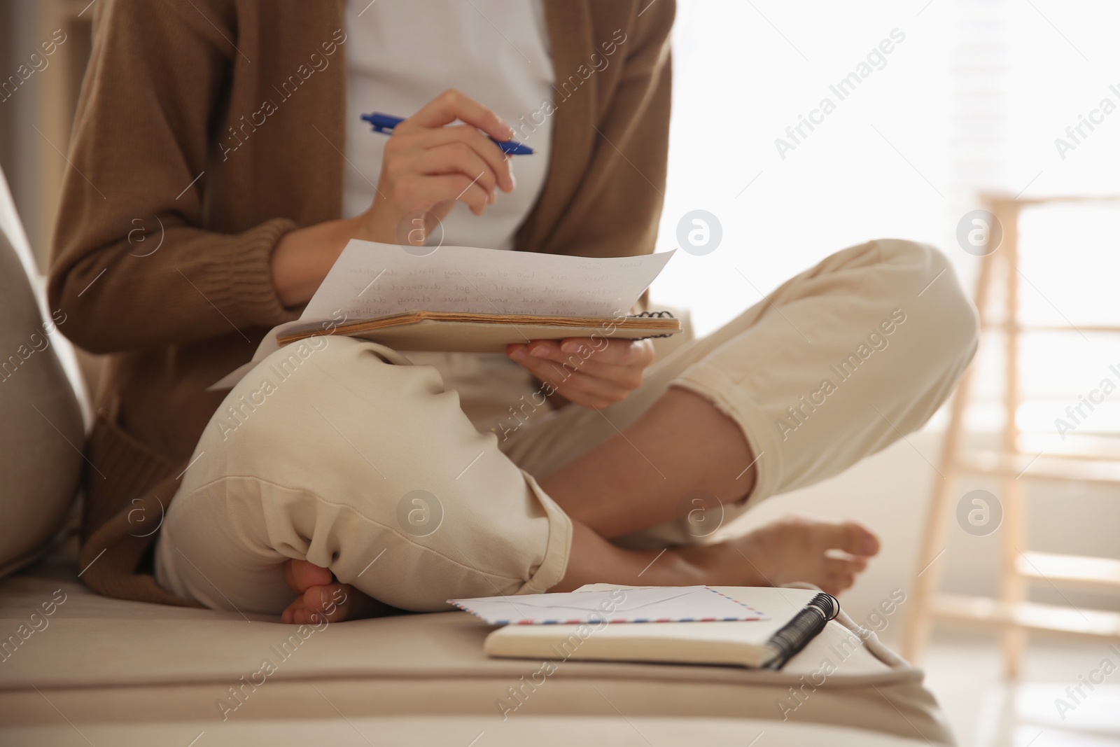 Photo of Woman writing letter while sitting on sofa at home, closeup