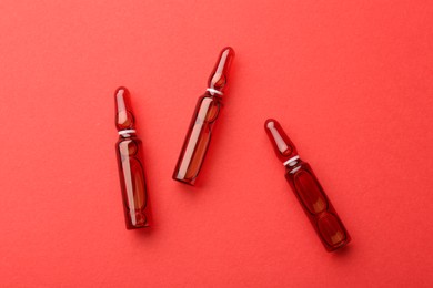 Photo of Glass ampoules with liquid on red background, top view