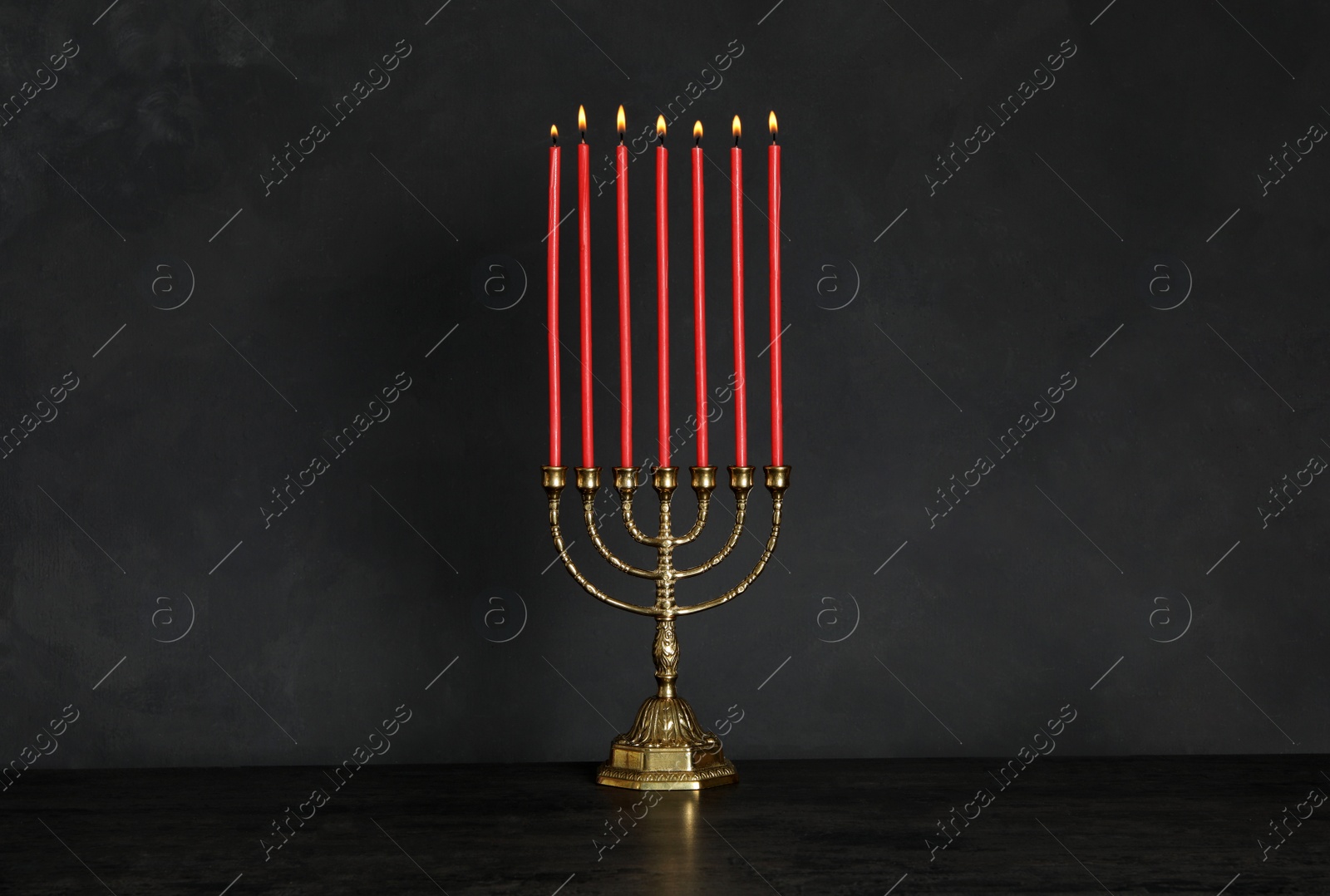 Photo of Golden menorah with burning candles on table against black background