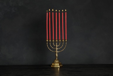 Photo of Golden menorah with burning candles on table against black background