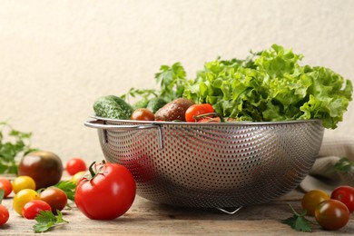 Wet vegetables in colander on wooden table, closeup