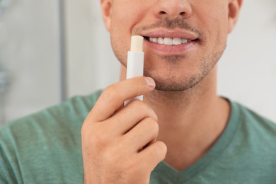 Photo of Man applying hygienic lip balm indoors, closeup