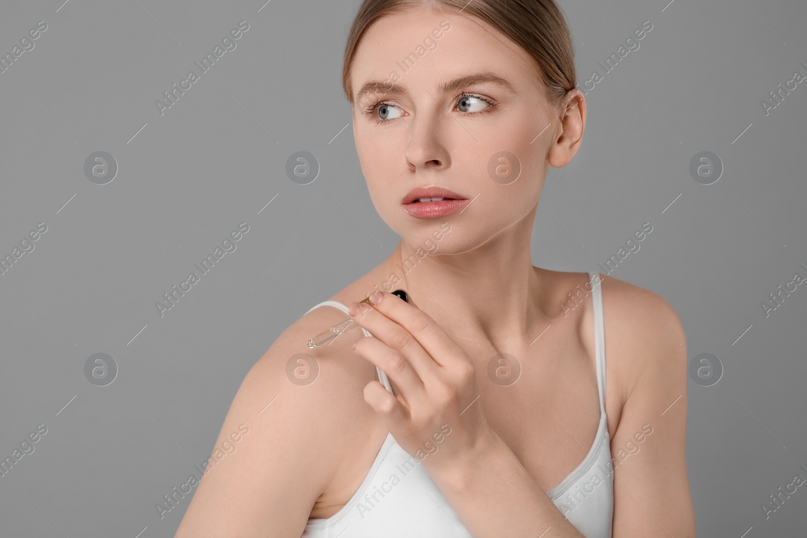 Photo of Beautiful young woman applying essential oil onto shoulder on grey background