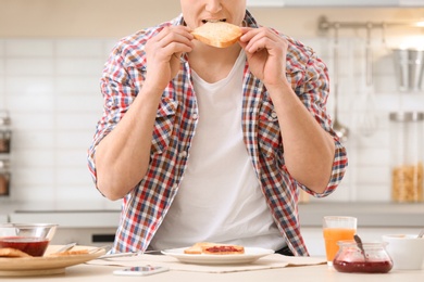 Photo of Young man eating tasty toasted bread at table in kitchen