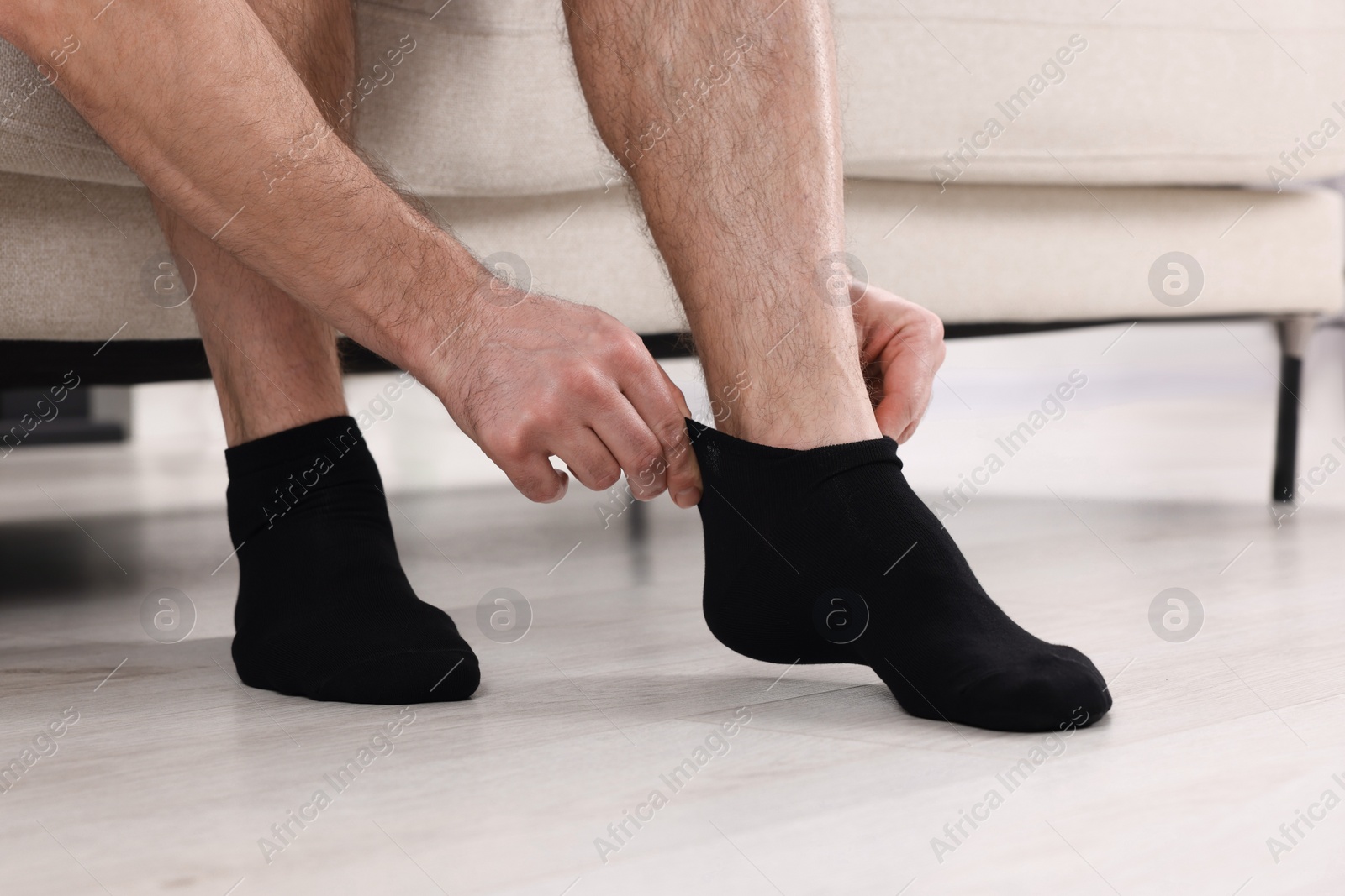 Photo of Man putting on black socks at home, closeup