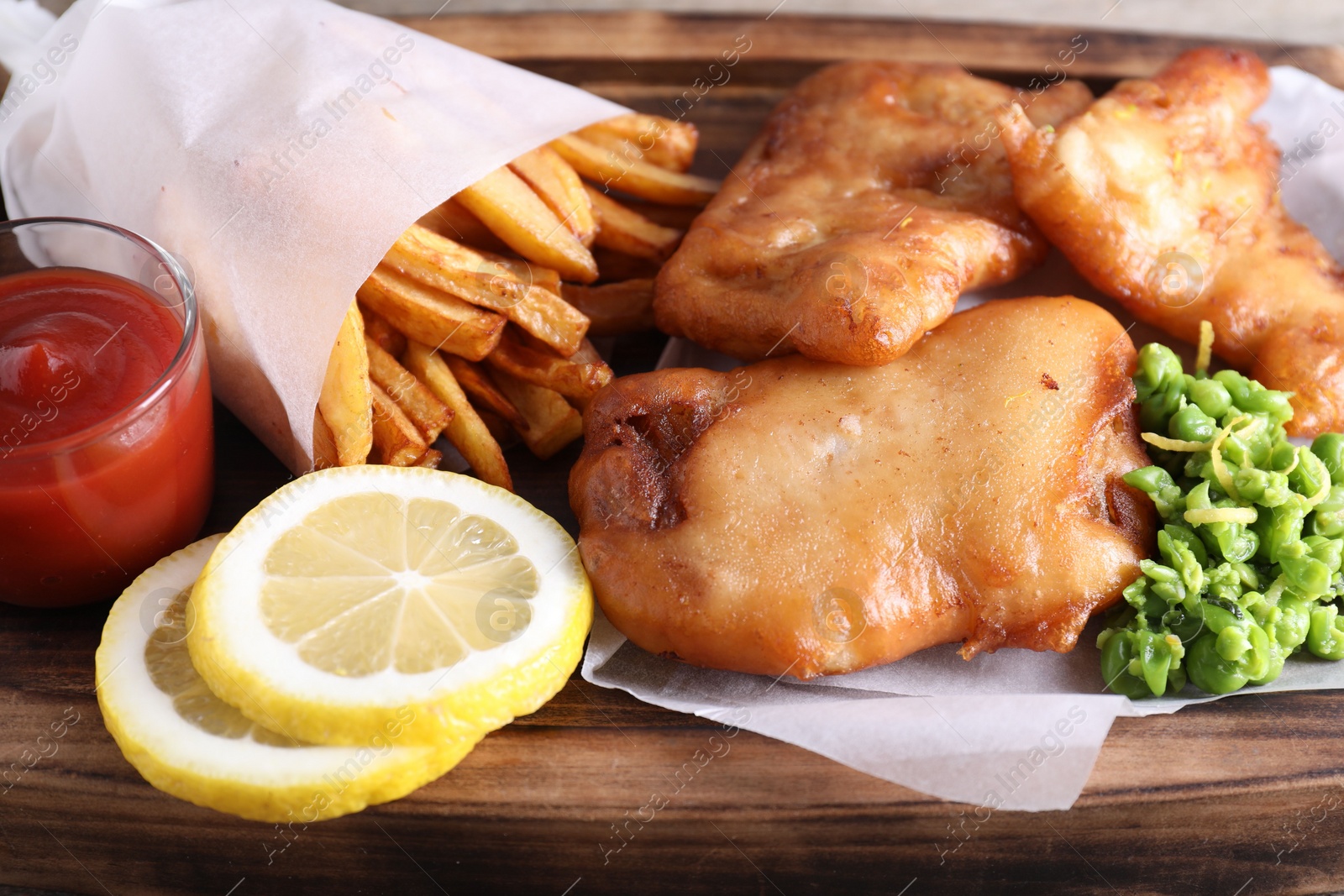 Photo of Tasty fish, chips, sauce and peas on wooden tray, closeup