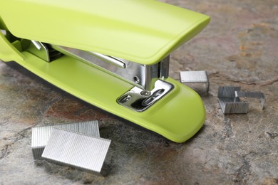 Green stapler with staples on stone textured surface, closeup