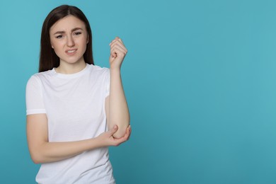 Photo of Young woman suffering from pain in her elbow on light blue background, space for text. Arthritis symptoms