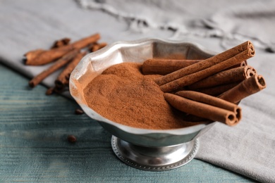 Photo of Bowl with aromatic cinnamon powder and sticks on wooden background