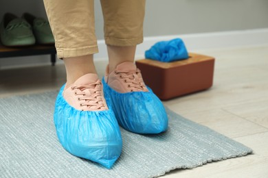 Woman wearing blue shoe covers onto her sneakers indoors, closeup