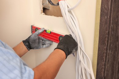 Photo of Electrician using spirit level indoors, closeup. Installation of electrical wiring