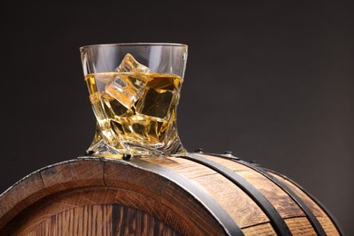 Photo of Whiskey with ice cube in glass on wooden barrel against gray background, space for text