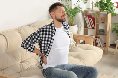 Photo of Man suffering from pain in back on sofa at home