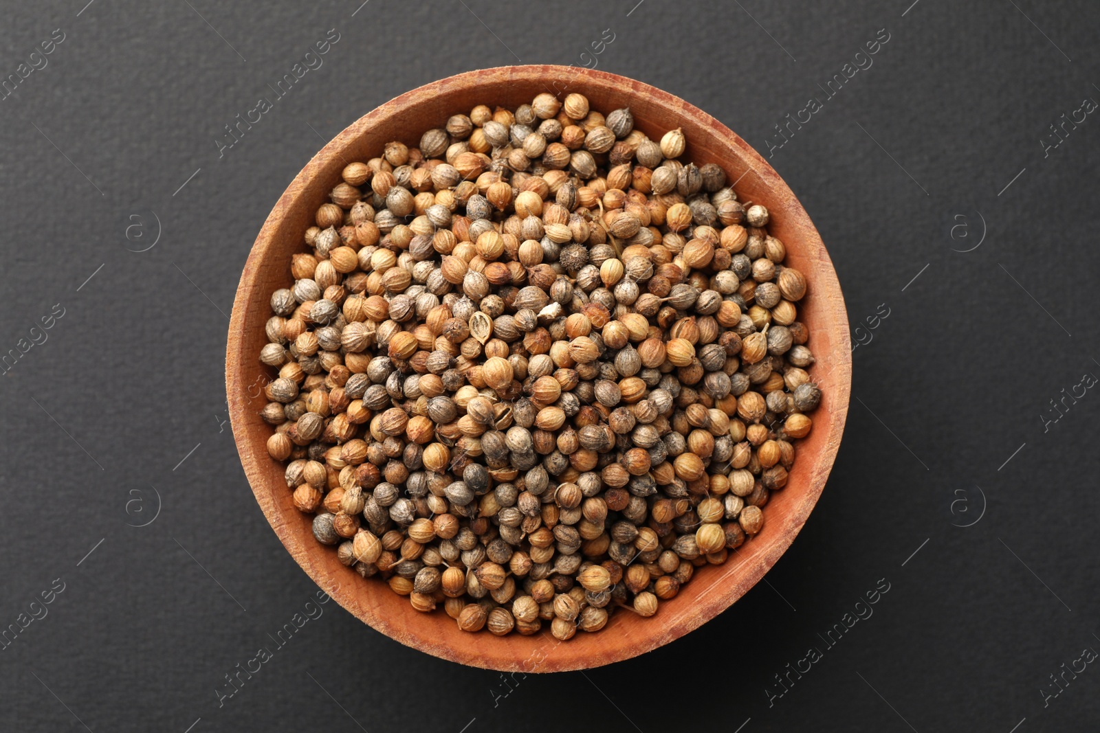 Photo of Wooden bowl of coriander grains on dark background, top view
