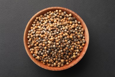 Photo of Wooden bowlcoriander grains on dark background, top view