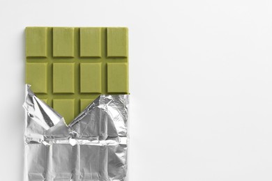 Photo of Tasty matcha chocolate bar wrapped in foil on white background, top view. Space for text