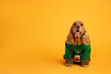 Photo of Adorable Cocker Spaniel in Christmas sweater on yellow background, space for text