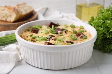 Photo of Tasty sausage casserole with green onion in baking dish on white tiled table, closeup