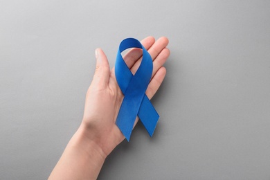 Photo of Woman holding blue awareness ribbon on grey background, top view