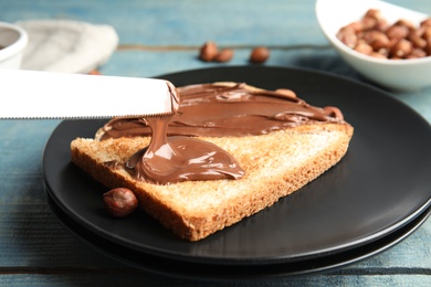 Photo of Spreading sweet chocolate cream onto toast on table, closeup