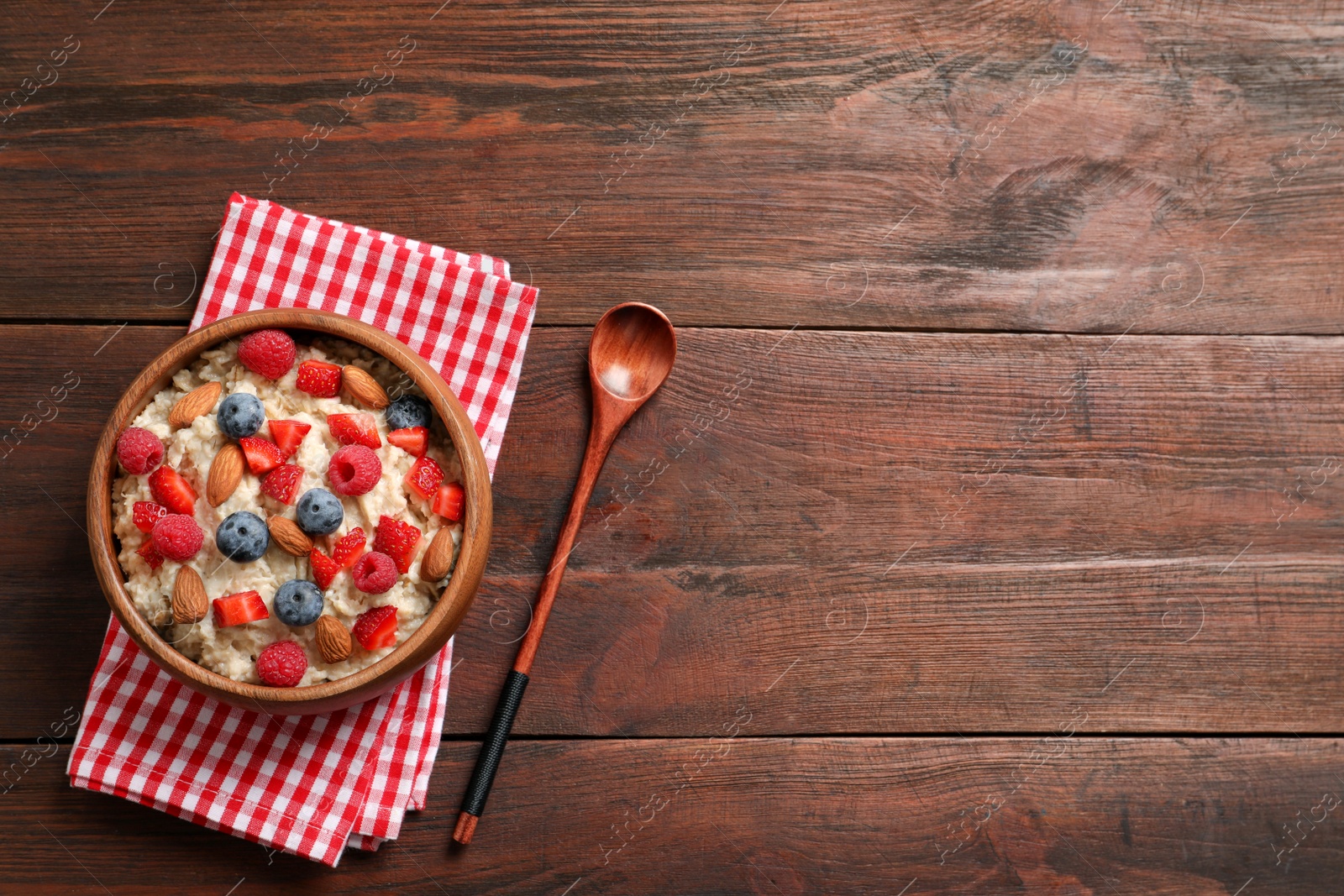 Photo of Tasty oatmeal porridge with berries and almond nuts served on wooden table, flat lay. Space for text