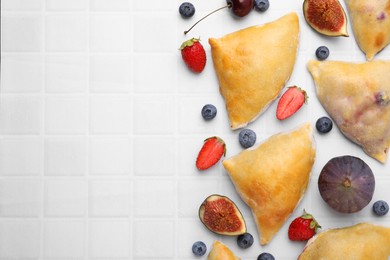 Photo of Delicious samosas, berries and fig on white tiled table, flat lay. Space for text
