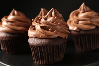 Delicious chocolate cupcakes with cream and beads on black table, closeup