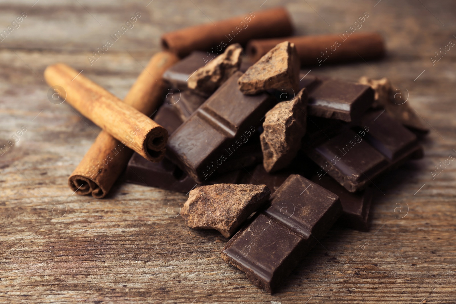 Photo of Pieces of delicious dark chocolate and cinnamon sticks on wooden table