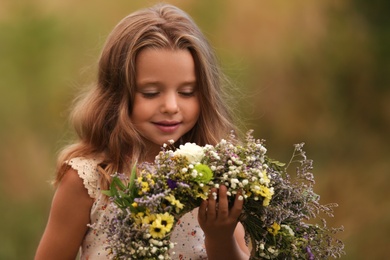 Cute little girl holding wreath made of beautiful flowers outdoors