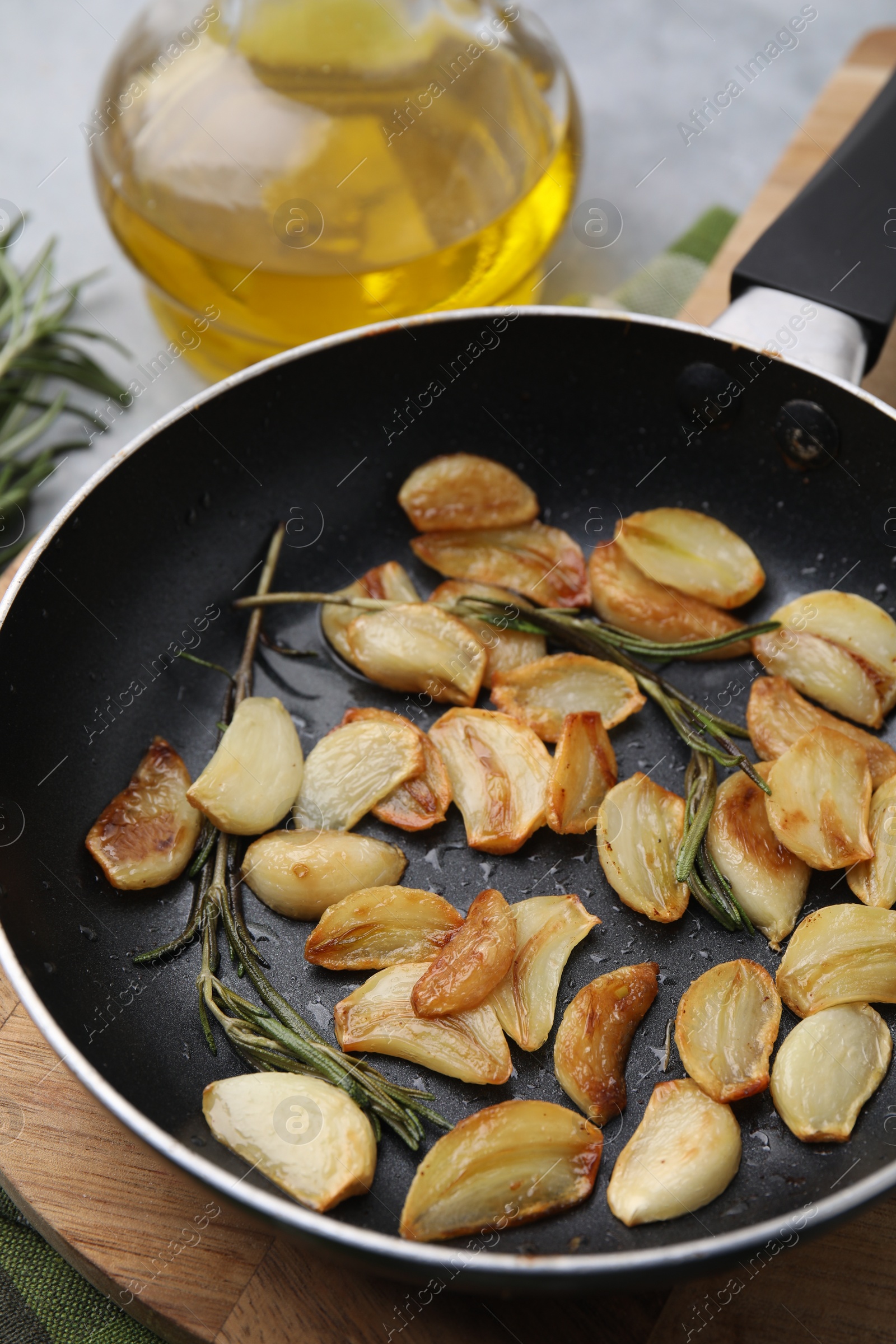 Photo of Frying pan with fried garlic cloves and rosemary on table