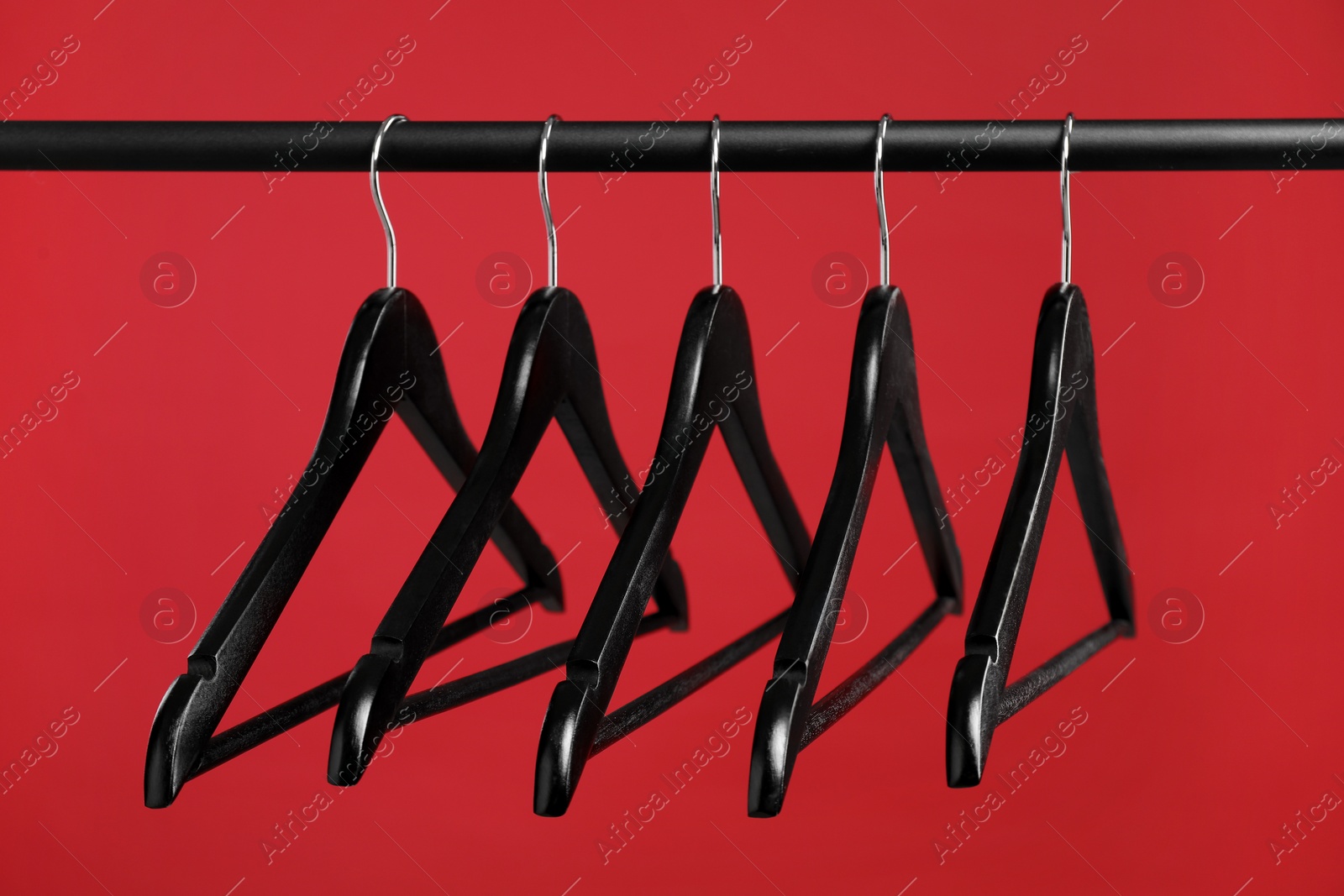 Photo of Black clothes hangers on rack against red background