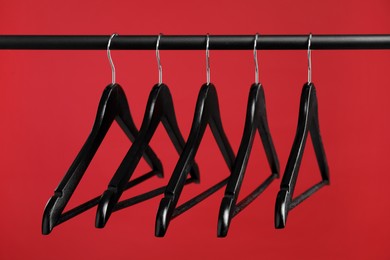 Photo of Black clothes hangers on rack against red background