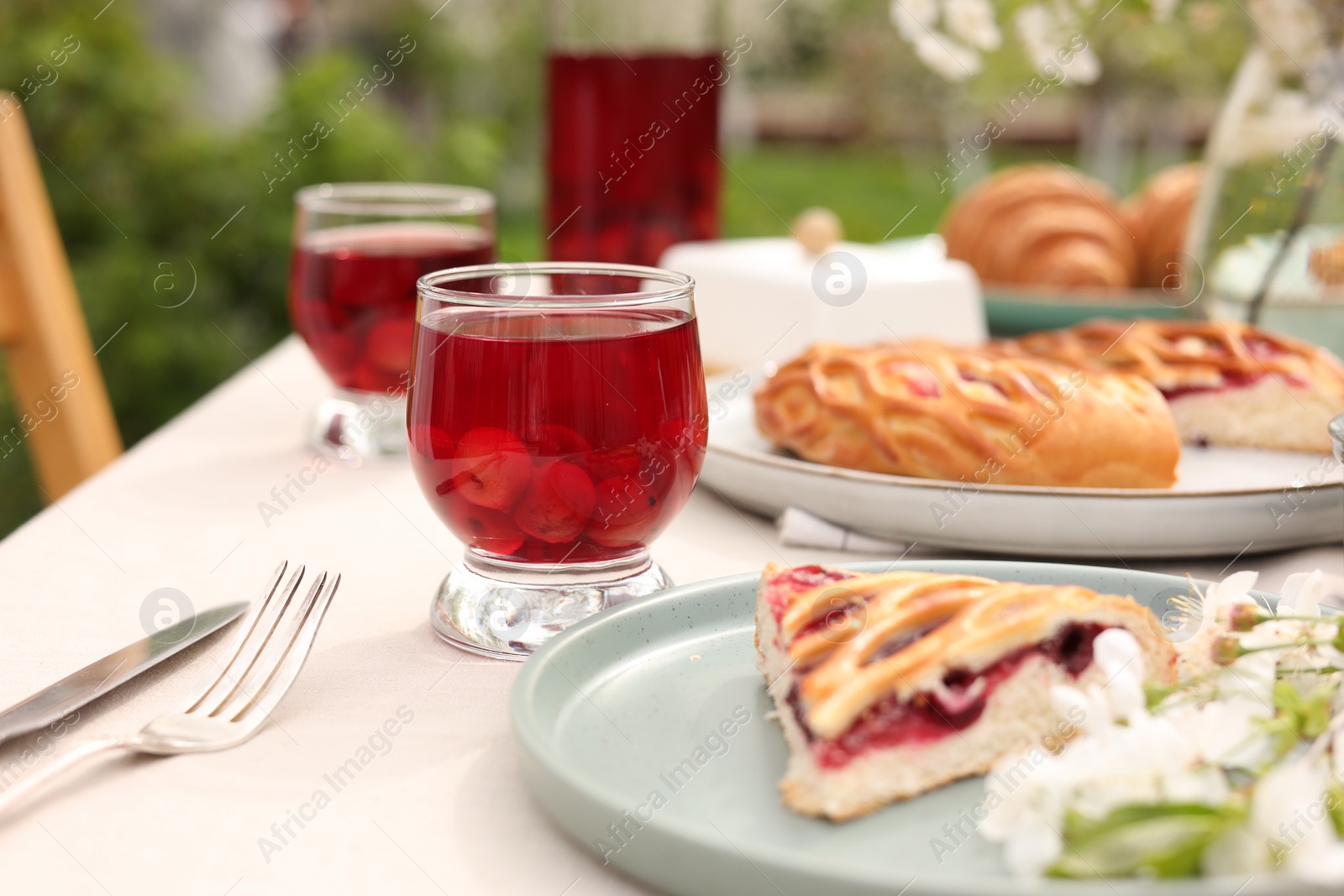 Photo of Stylish table setting with beautiful spring flowers, fruit drink and pie in garden