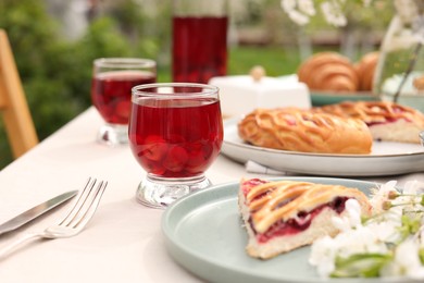 Stylish table setting with beautiful spring flowers, fruit drink and pie in garden