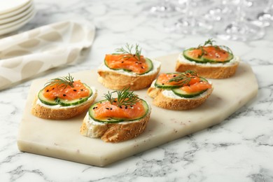 Photo of Tasty canapes with salmon, cucumber and cream cheese on white marble table