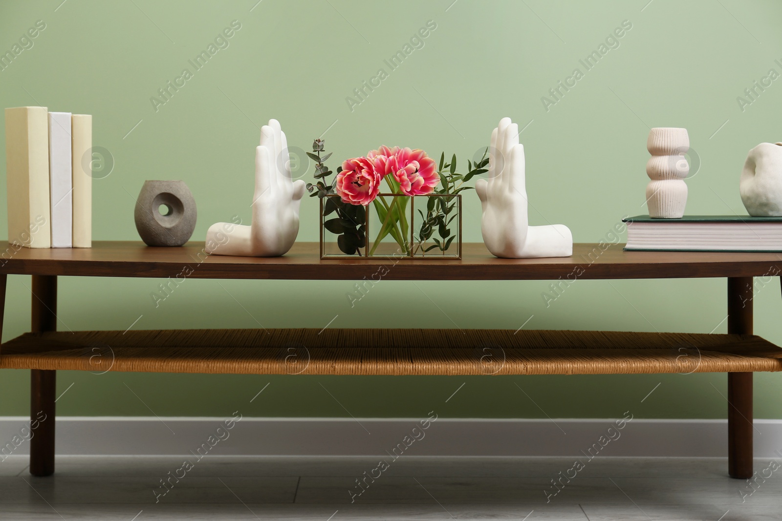 Photo of Wooden coffee table with flowers and decor elements near pale green wall indoors. Stylish interior design