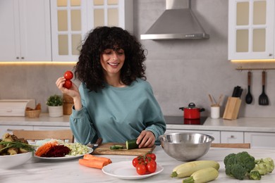 Photo of Woman cooking healthy vegetarian meal at white marble table in kitchen