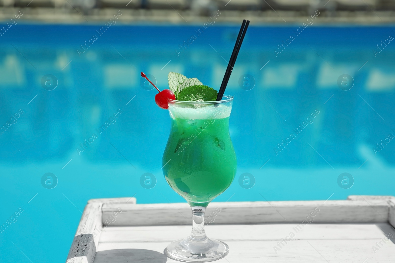 Photo of Refreshing cocktail on wooden table near swimming pool outdoors