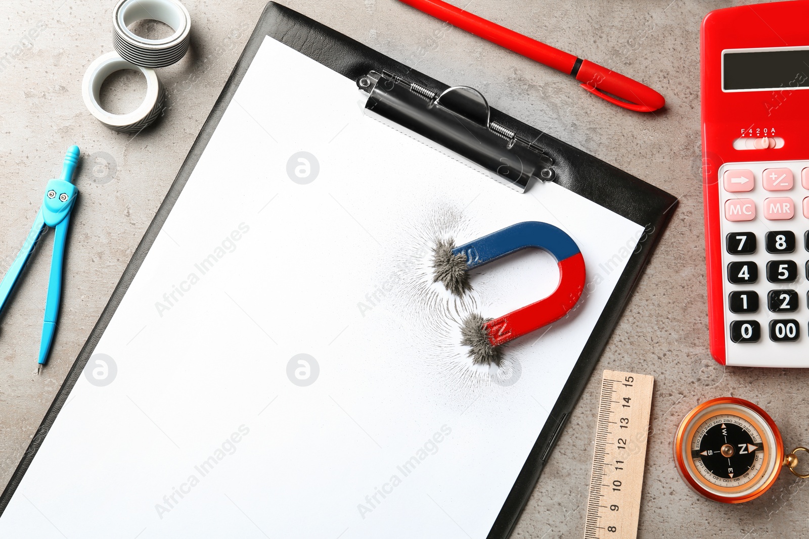 Photo of Clipboard, stationery and magnet with iron powder on table, top view. Space for text