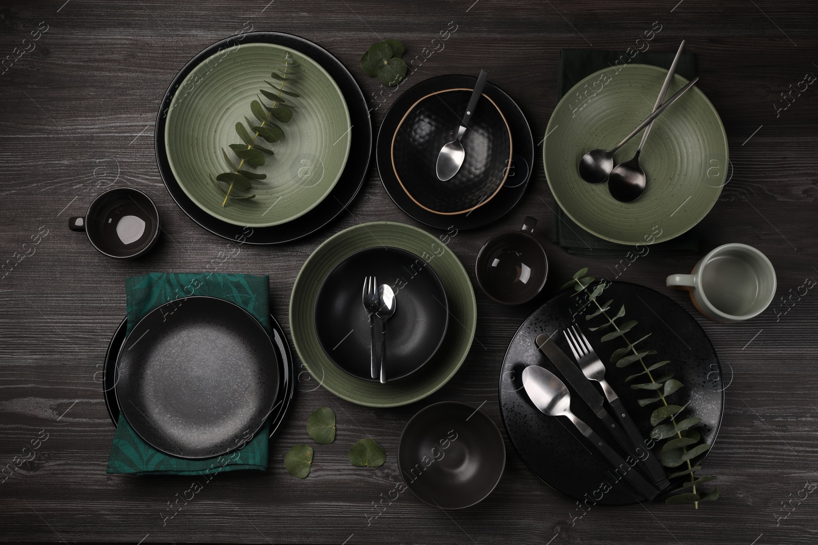 Photo of Stylish table setting with cutlery and eucalyptus branches on dark wooden background, flat lay